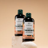 Two bottles of The Body Shop Pink Grapefruit Shower Gel 250 ML positioned on decorative stones against a soft beige backgroun