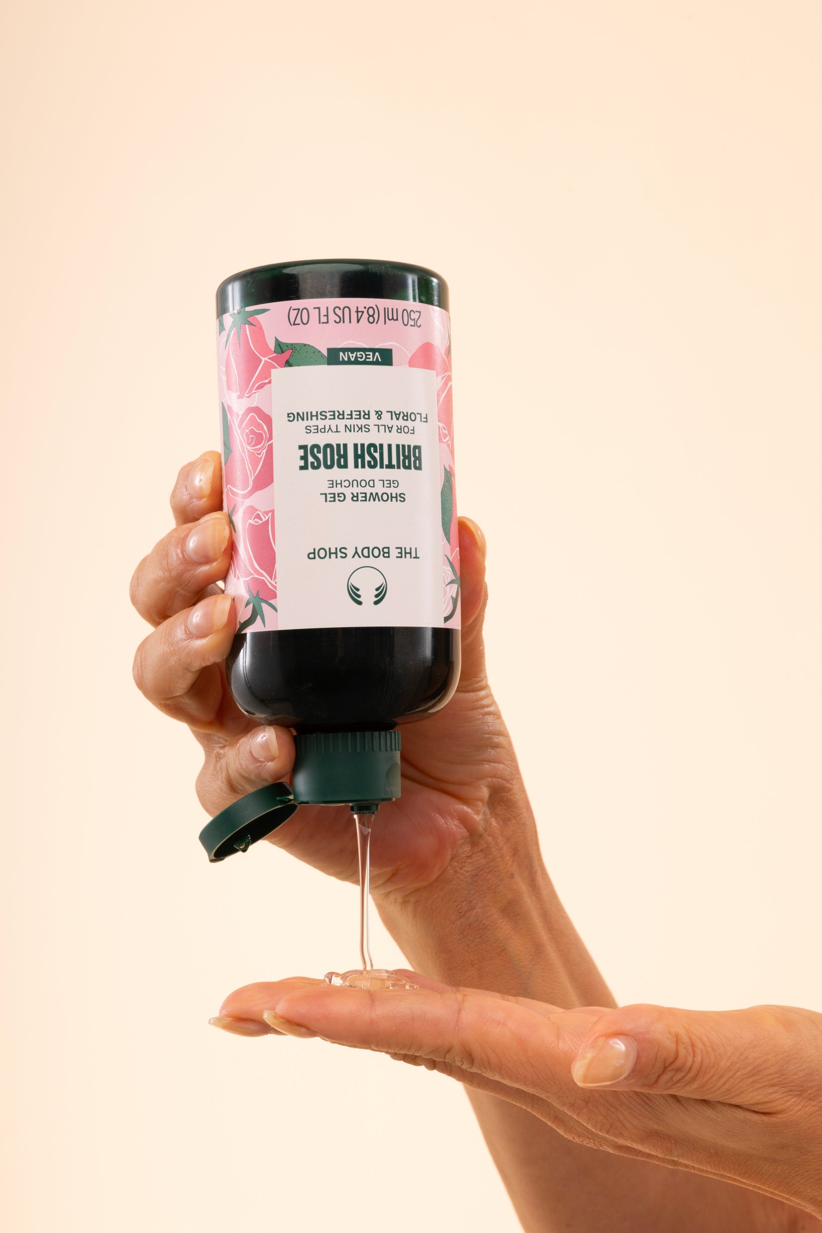 Hands dispensing The Body Shop British Rose Shower Gel 250ml, showing product texture against soft background.