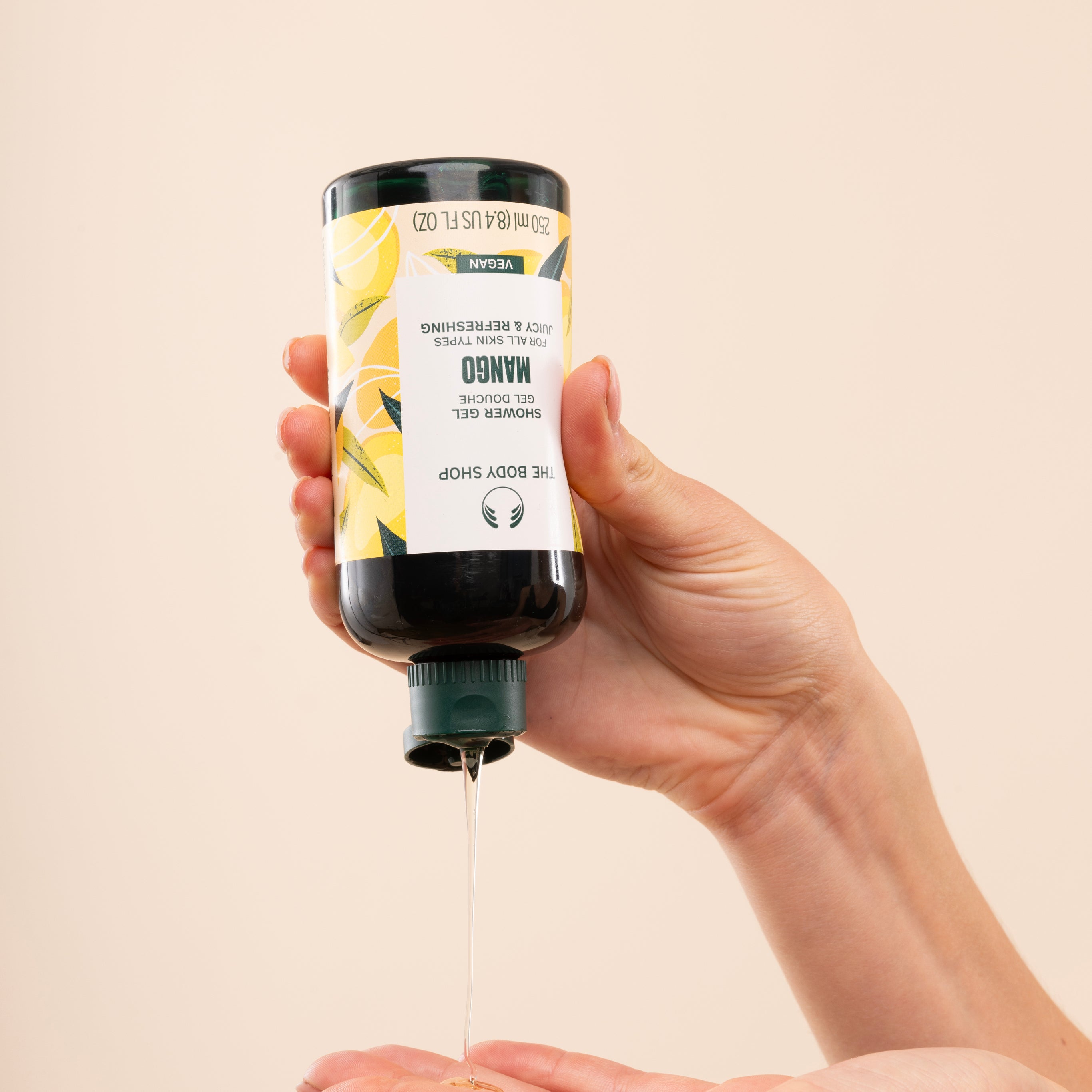Person dispensing The Body Shop Mango Shower Gel 250 ML against soft beige background