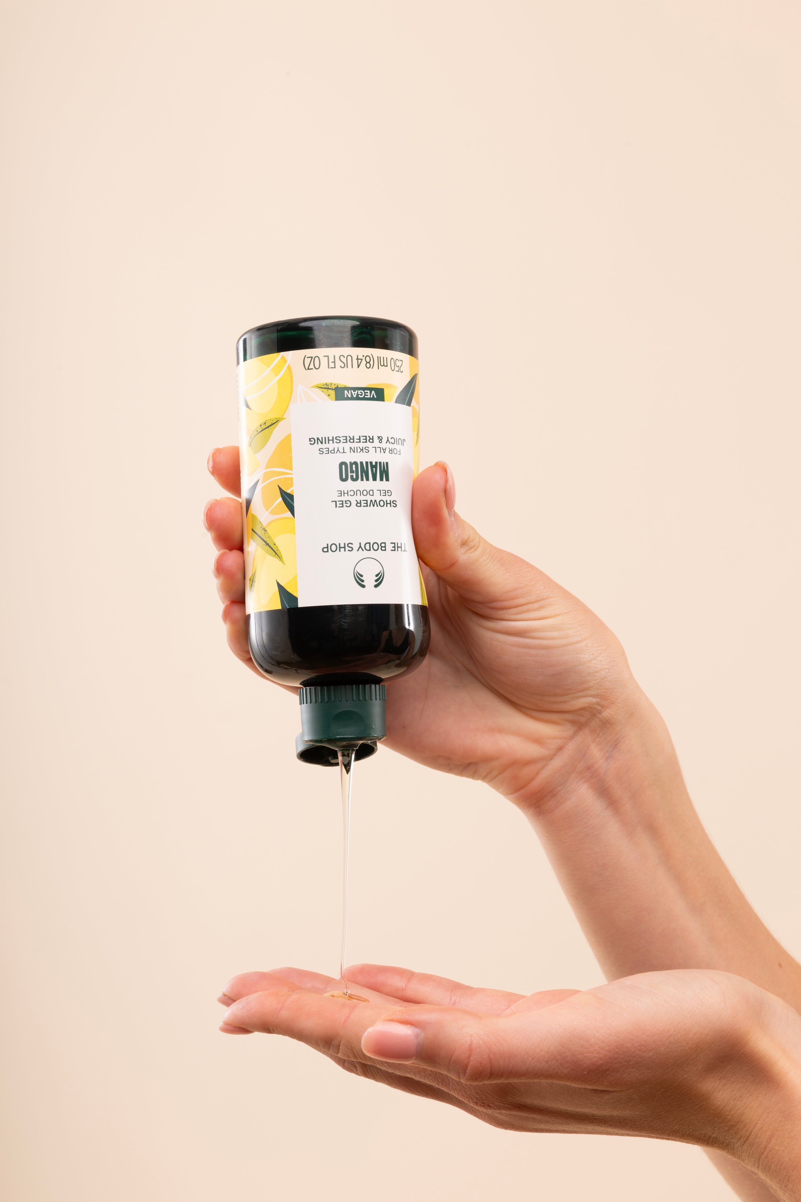 Person dispensing The Body Shop Mango Shower Gel 250 ML against soft beige background