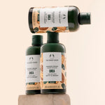 Three bottles of The Body Shop Shea Shower Cream 250ml elegantly stacked on a textured stone pedestal against a soft pastel b