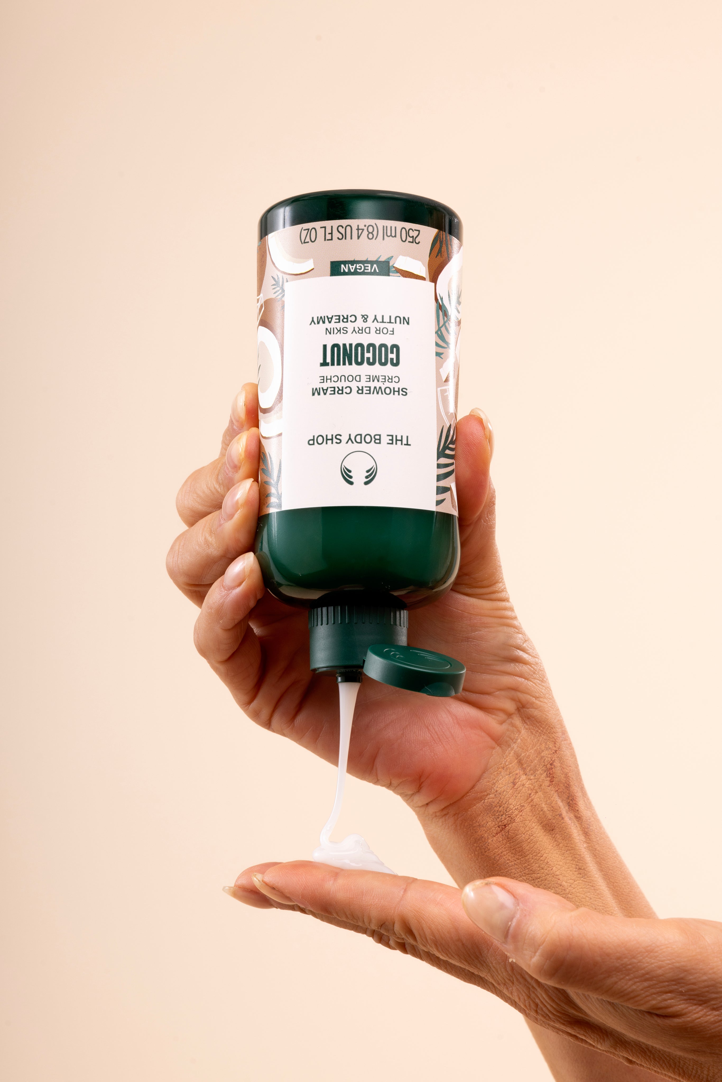 Hand dispensing The Body Shop Coconut Shower Cream 250 ML into palm, in relaxing bathroom setting