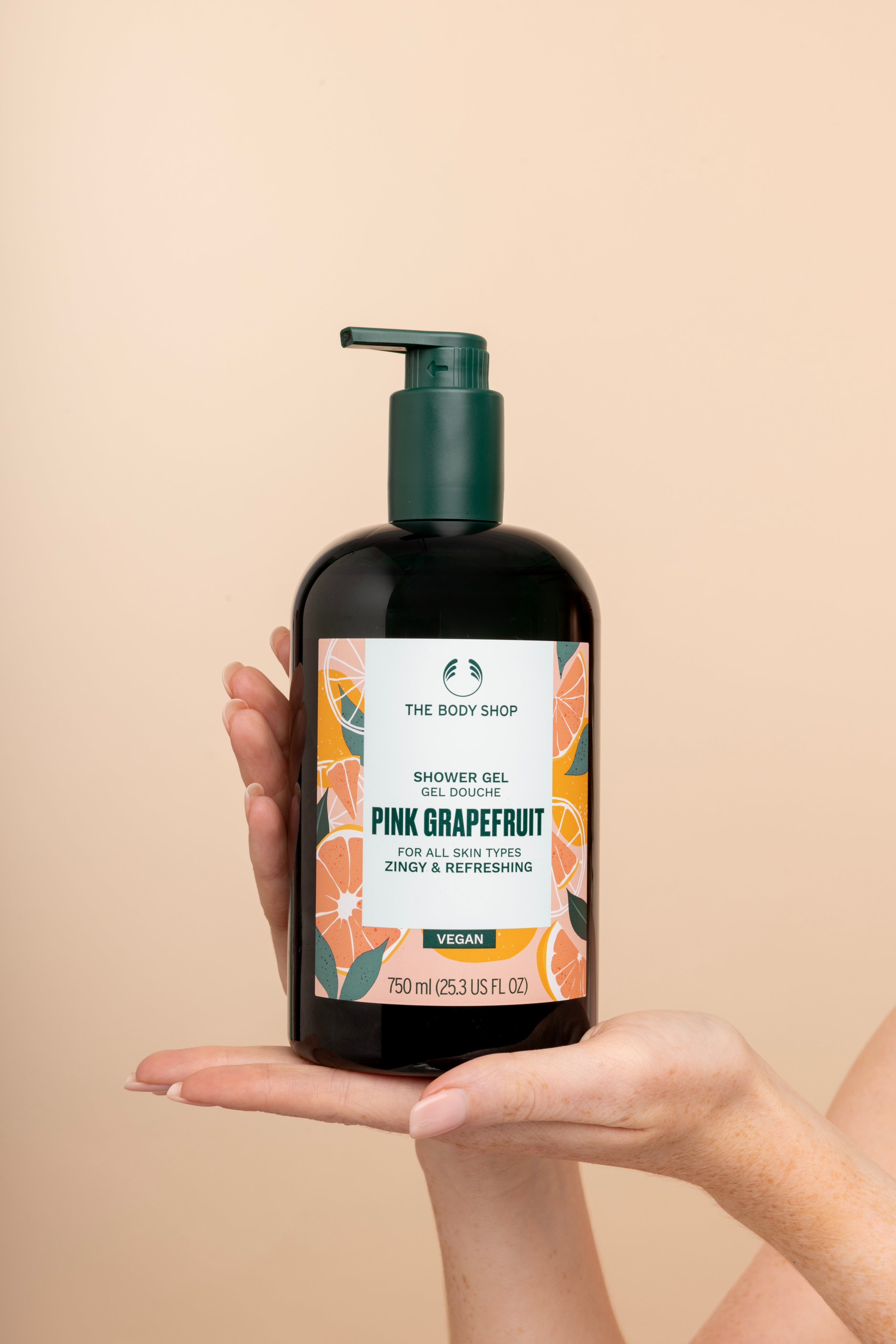 Hand holding The Body Shop Pink Grapefruit Shower Gel 750 ML against soft, neutral background