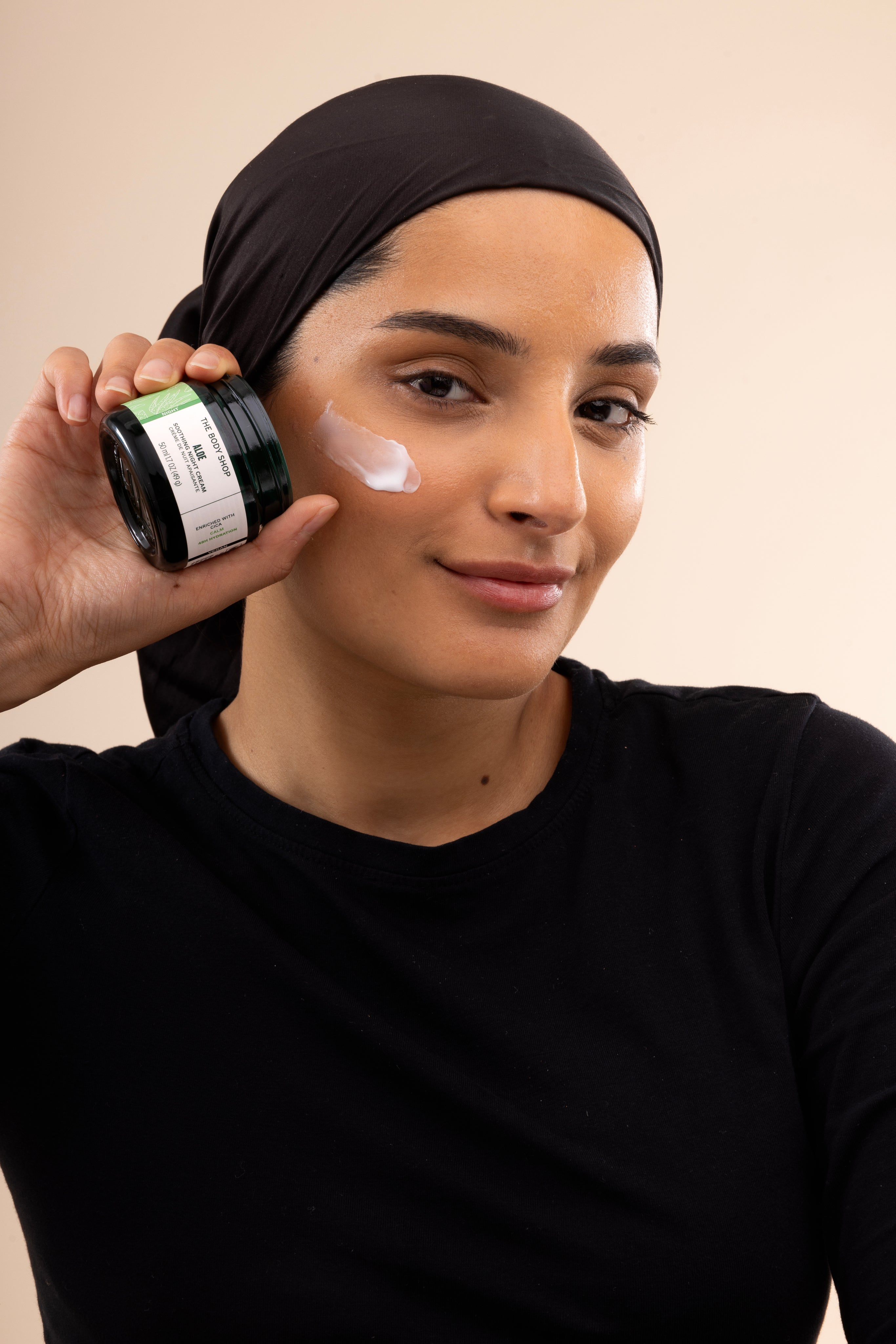 Woman applying The Body Shop Aloe Soothing Night Cream 50ml in a studio setting with a soft backdrop.