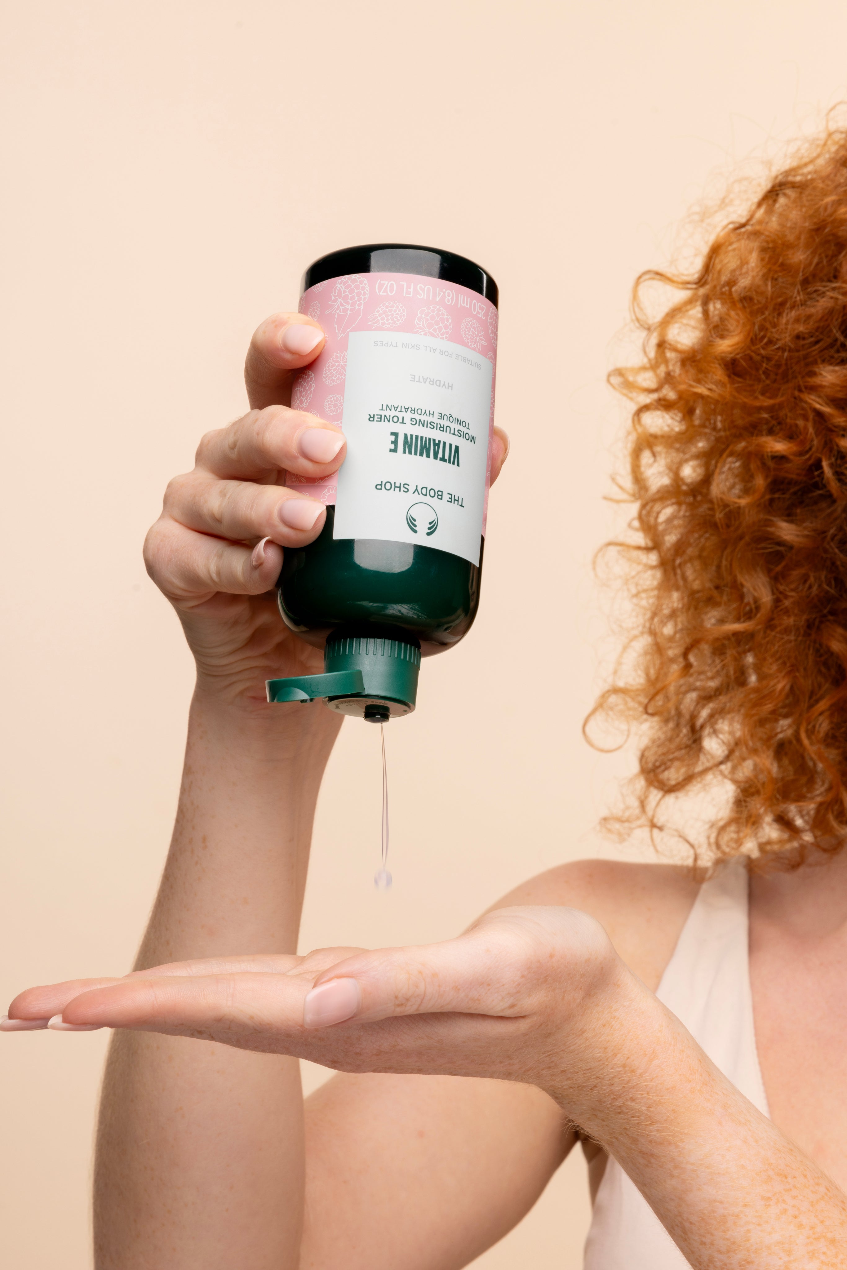 Person dispensing The Body Shop Vitamin E Moisturising Toner 250 ML in studio setting with backdrop