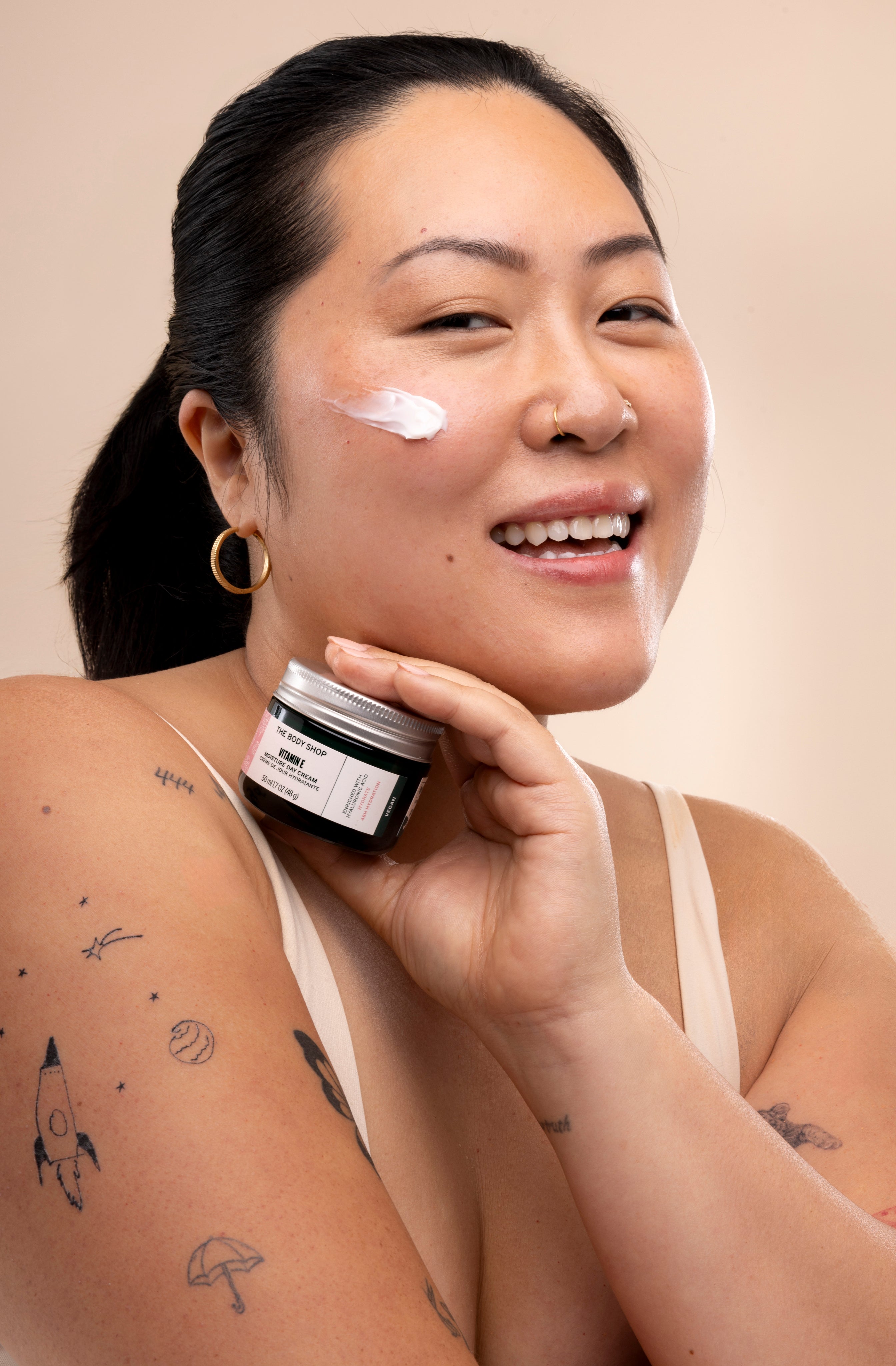 Woman applying The Body Shop Vitamin E Moisture Cream in a well-lit setting with a soft background