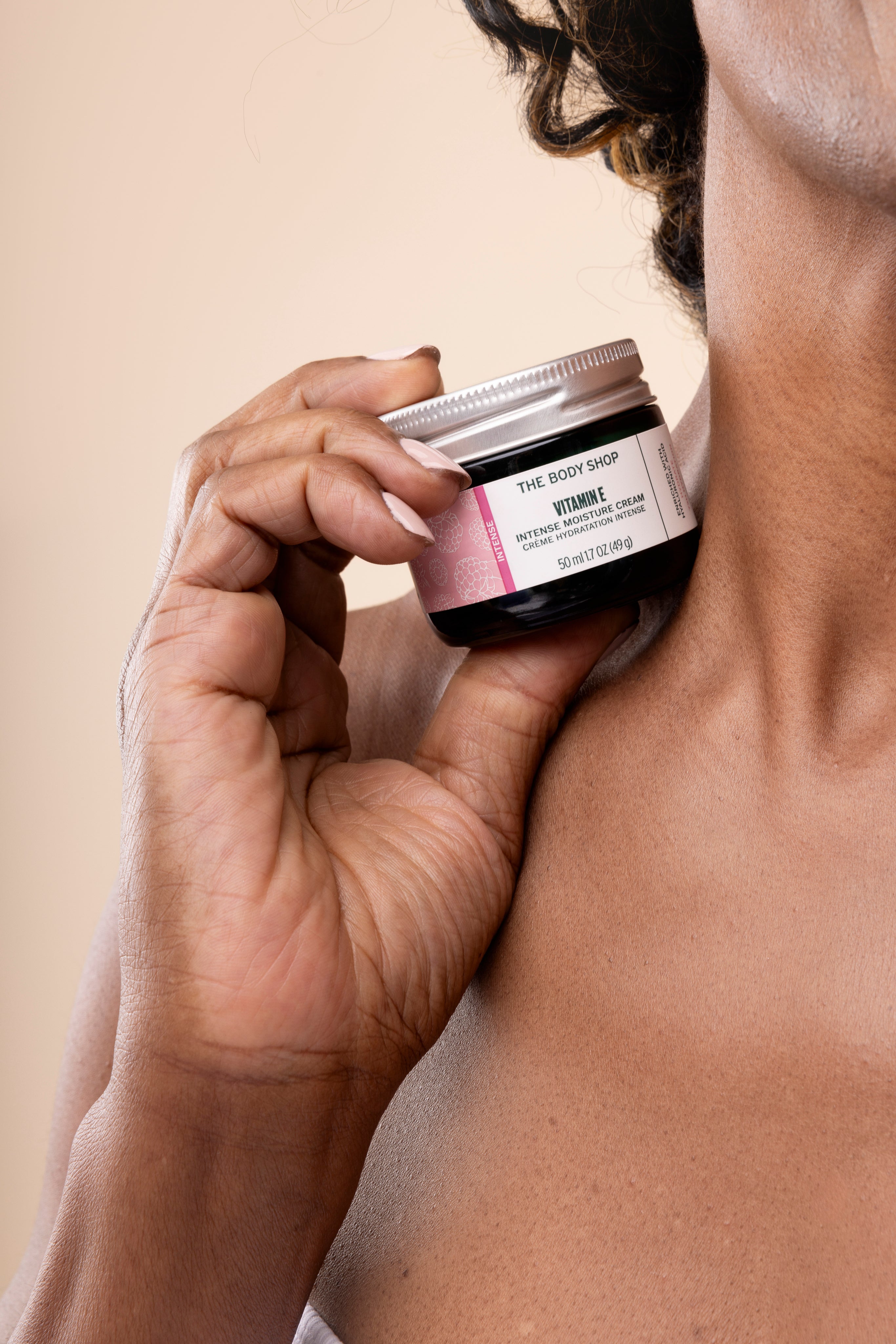 Woman holding The Body Shop Vitamin E Intense Moisture Cream 50 ML against skin in a studio setting