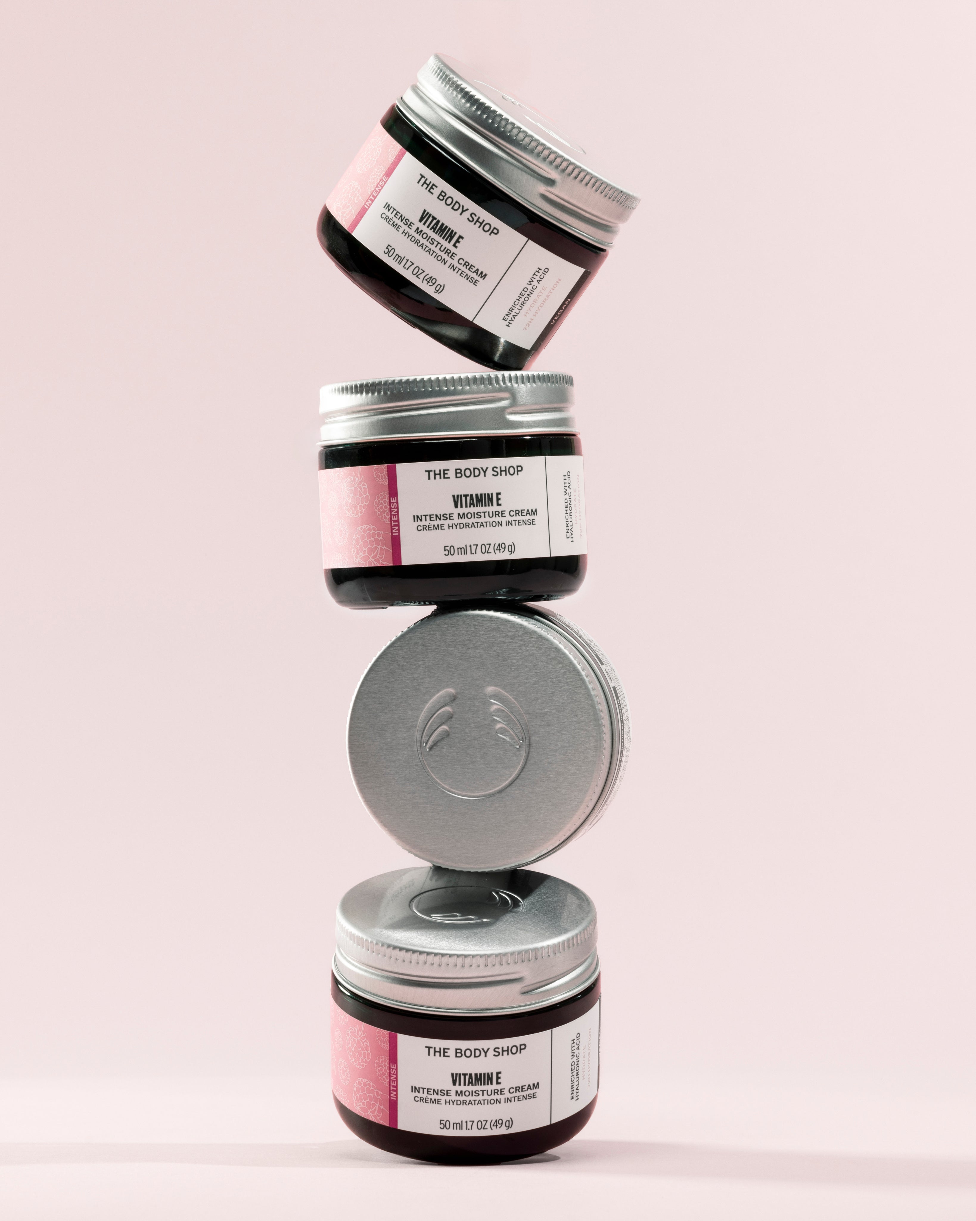 Stack of The Body Shop Vitamin E Intense Moisture Cream 50 ML jars against a soft pink background