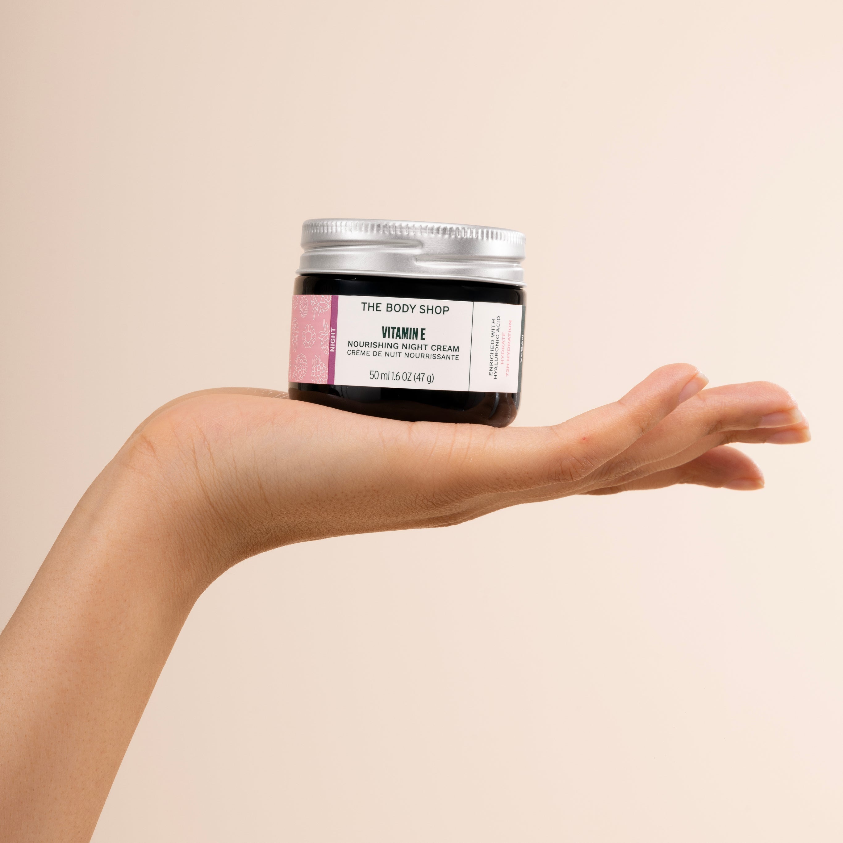 Person holding The Body Shop Vitamin E Nourishing Night Cream 50 ML against soft beige background