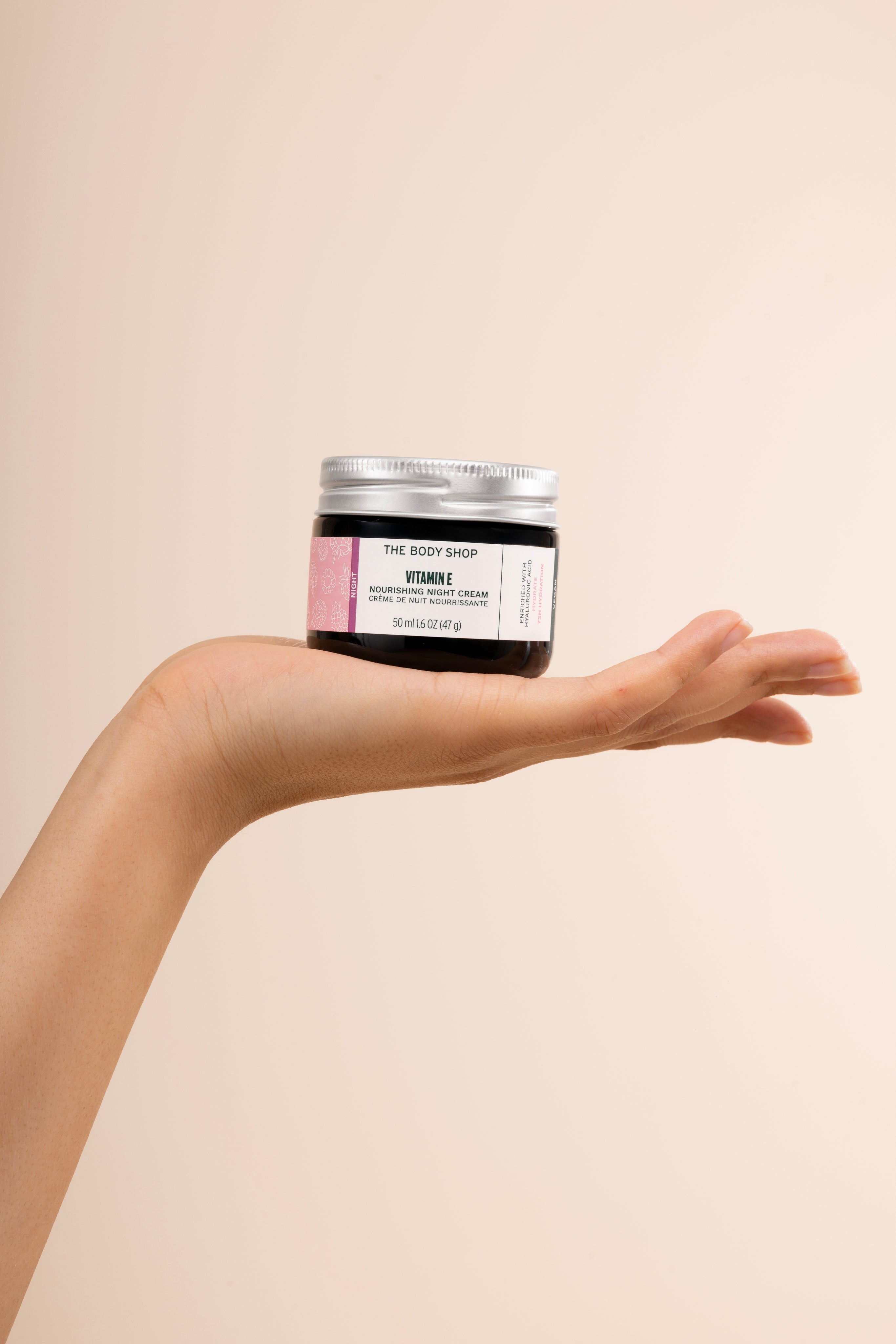 Person holding The Body Shop Vitamin E Nourishing Night Cream 50 ML against soft beige background