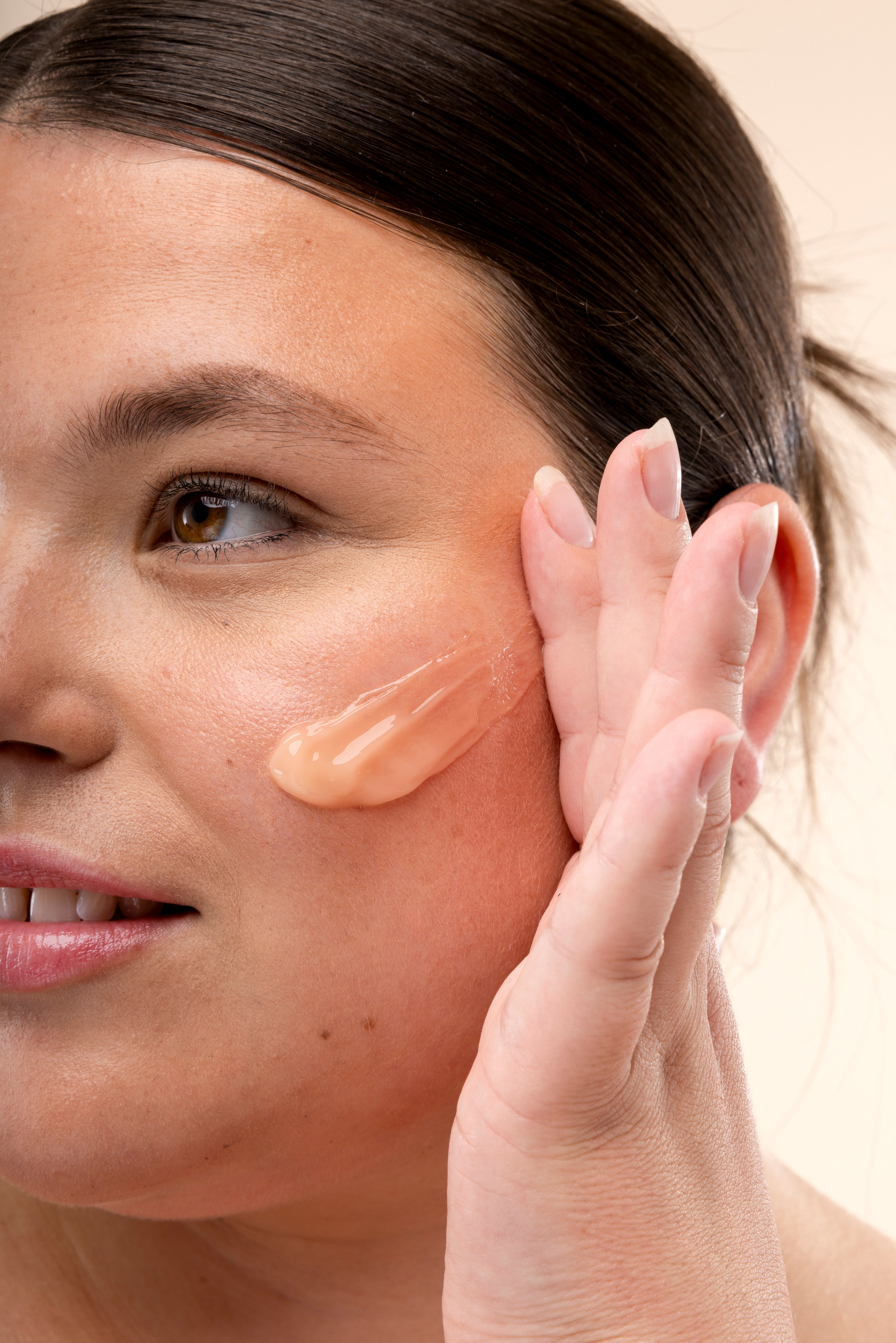 A person applies a cream to their cheek against a plain background.