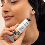 Woman holding The Body Shop Shea Hand Balm 30ml, applying it on her skin in a studio setting with backdrop.