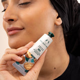 Woman holding The Body Shop Shea Hand Balm 30ml, applying it on her skin in a studio setting with backdrop.