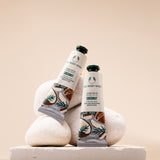 Two tubes of The Body Shop Coconut Hand Balm 30ml elegantly displayed on smooth stones against a soft, neutral backdrop.