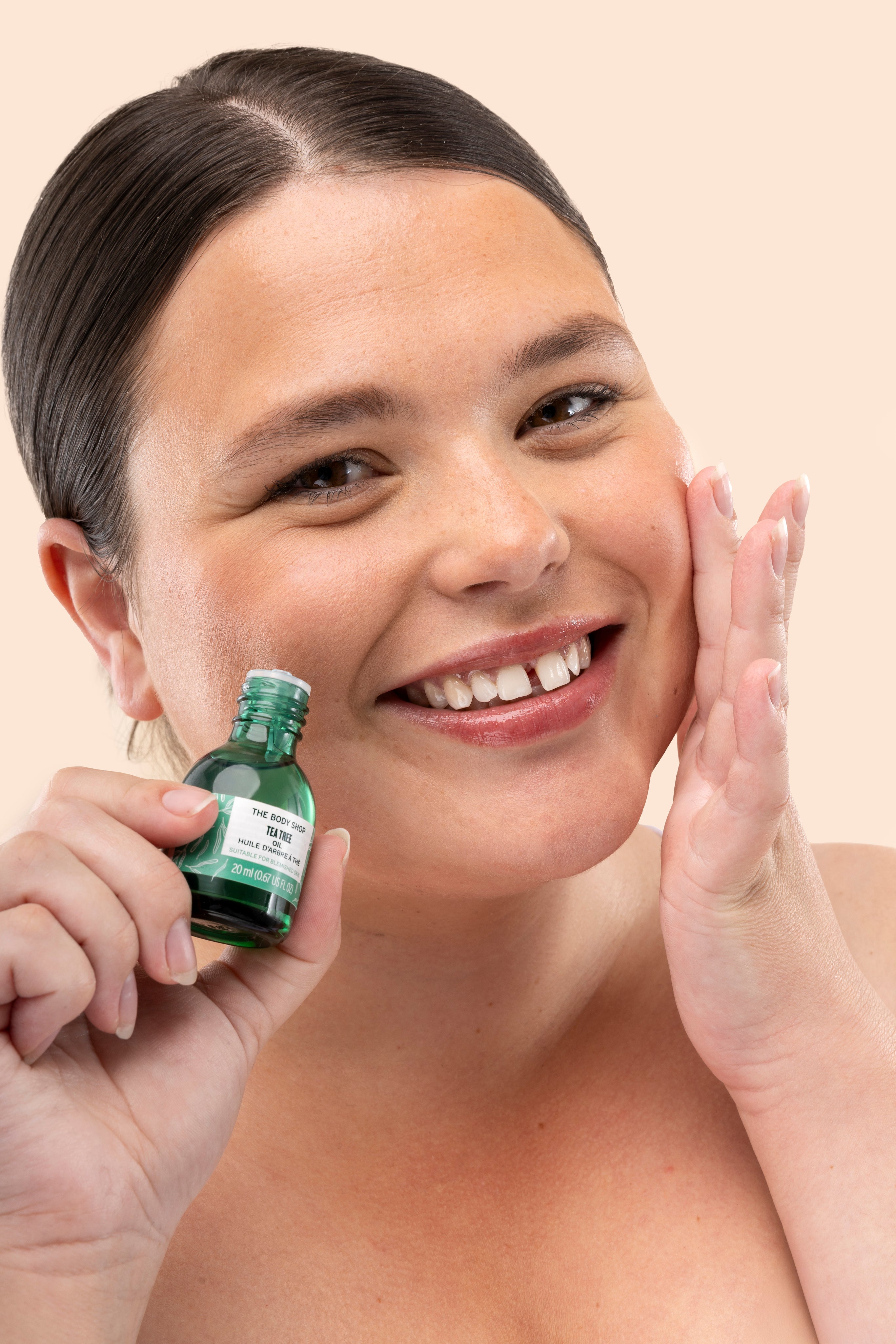 Woman applying The Body Shop Tea Tree Oil 20 ML, with green bottle, in bathroom setting
