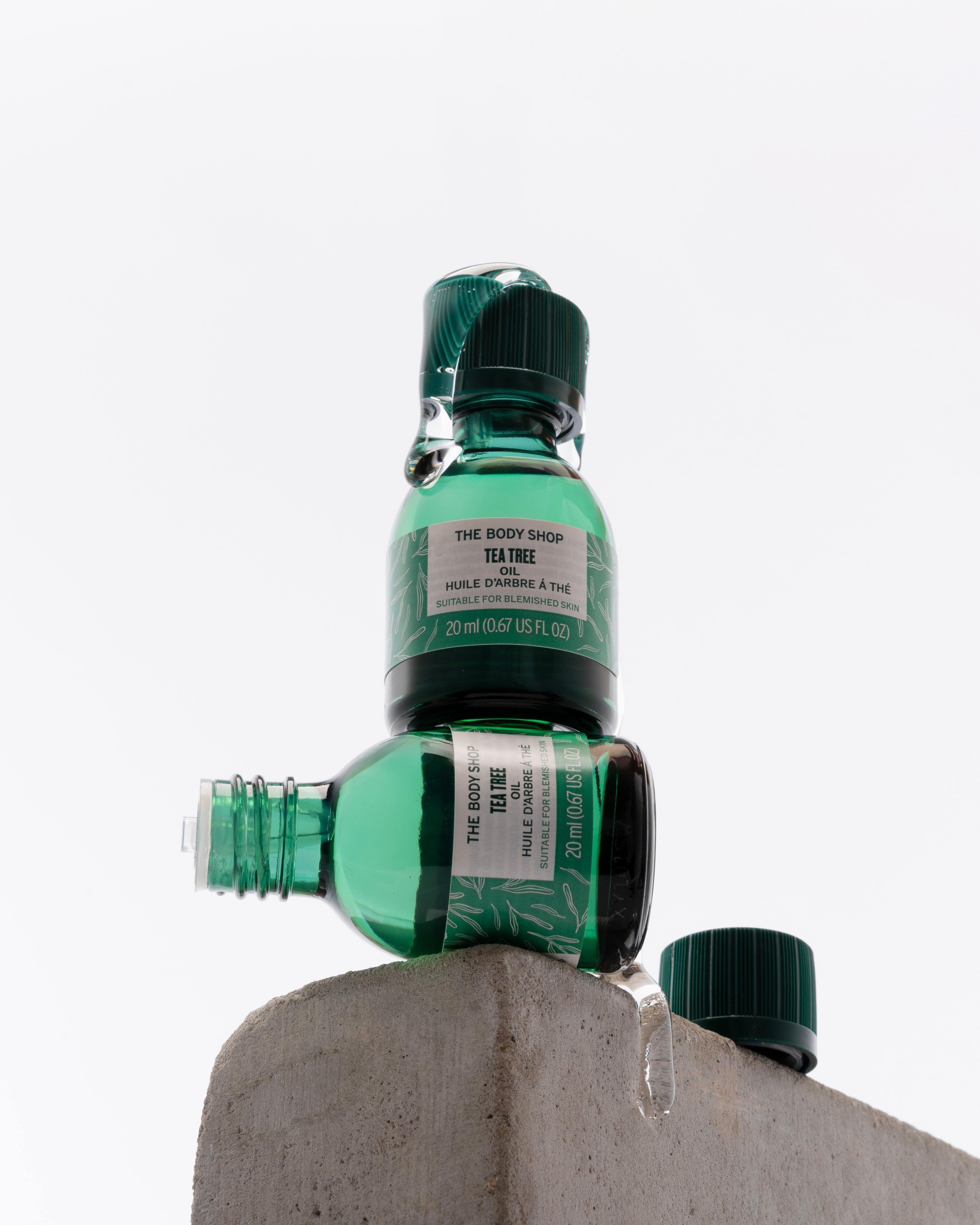 Stack of The Body Shop Tea Tree Oil 20 ML on concrete block, showcasing vibrant green branding against clean background