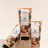 Three tubes of The Body Shop Shea Body Lotion 200 ML artistically arranged on a stone surface against a soft, muted backgroun