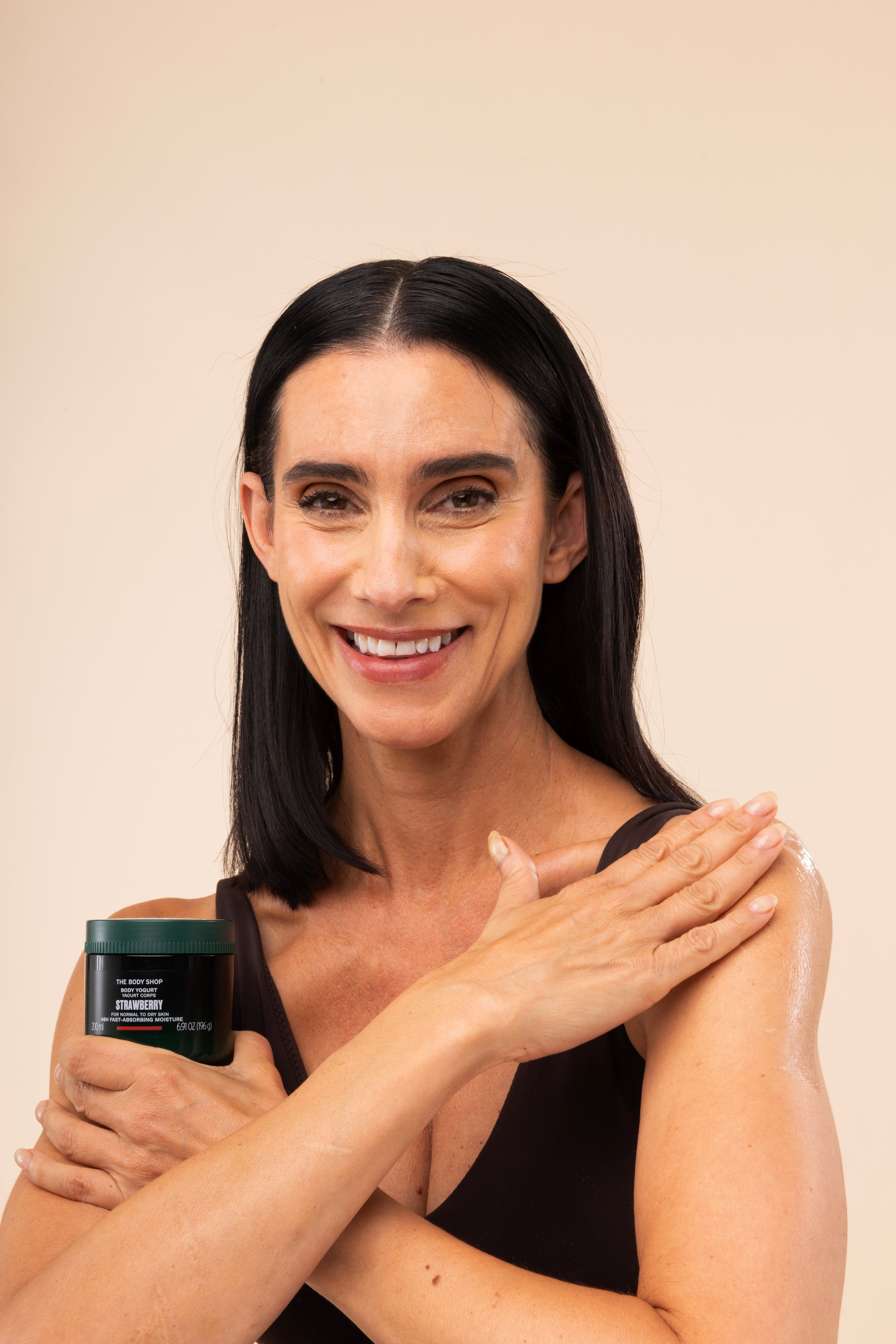 Woman applying The Body Shop Strawberry Body Yogurt 650g on her arm against a soft, neutral background.