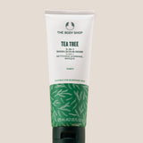A tube of The Body Shop Tea Tree 3-in-1 Wash, Scrub, Mask 125ml displayed on a stone pedestal with a soft beige background.