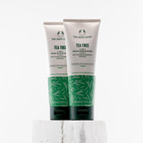 Two tubes of The Body Shop Tea Tree 3-in-1 Wash-Scrub-Mask 125ml displayed on a textured pedestal against a clean background.
