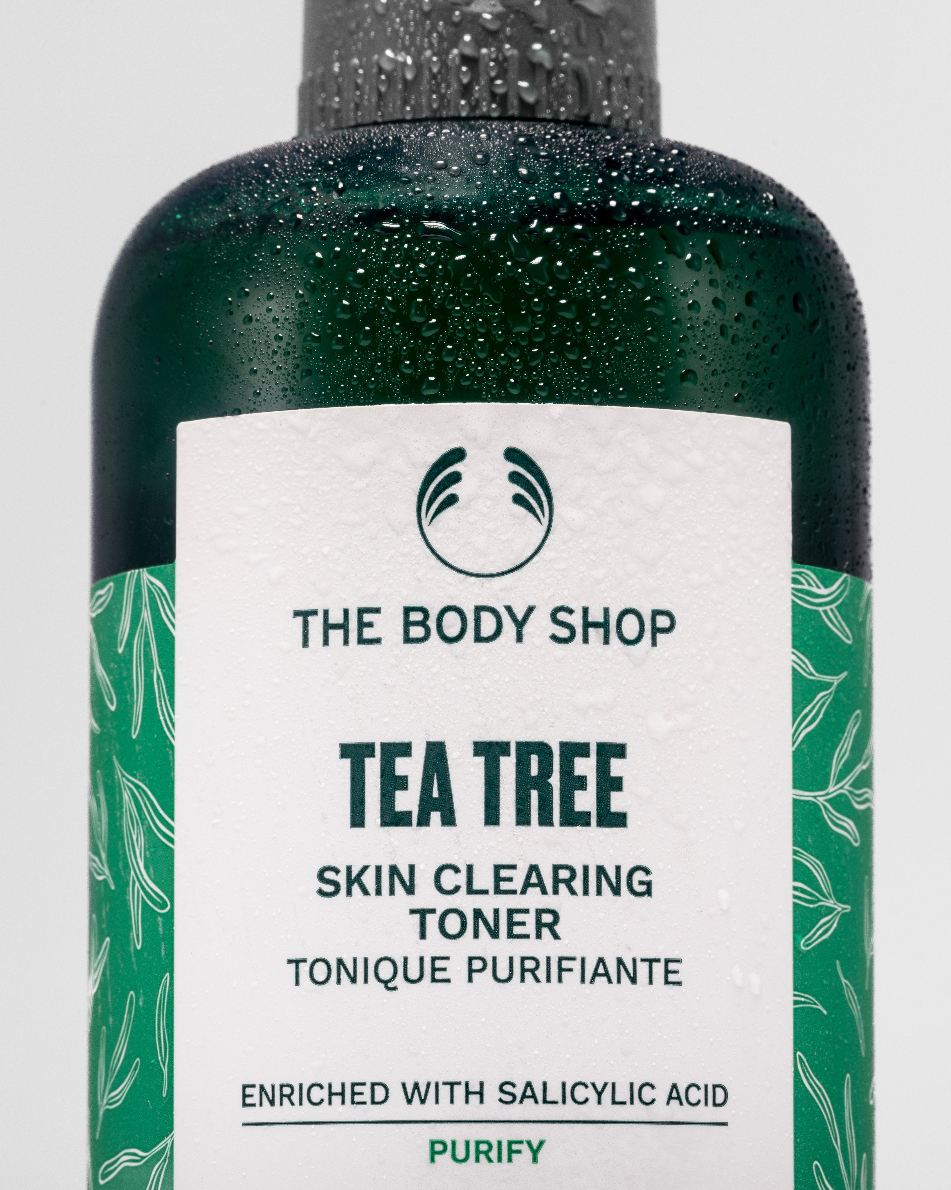 Close-up of The Body Shop Tea Tree Skin Clearing Toner, droplets on bottle against clean backdrop.