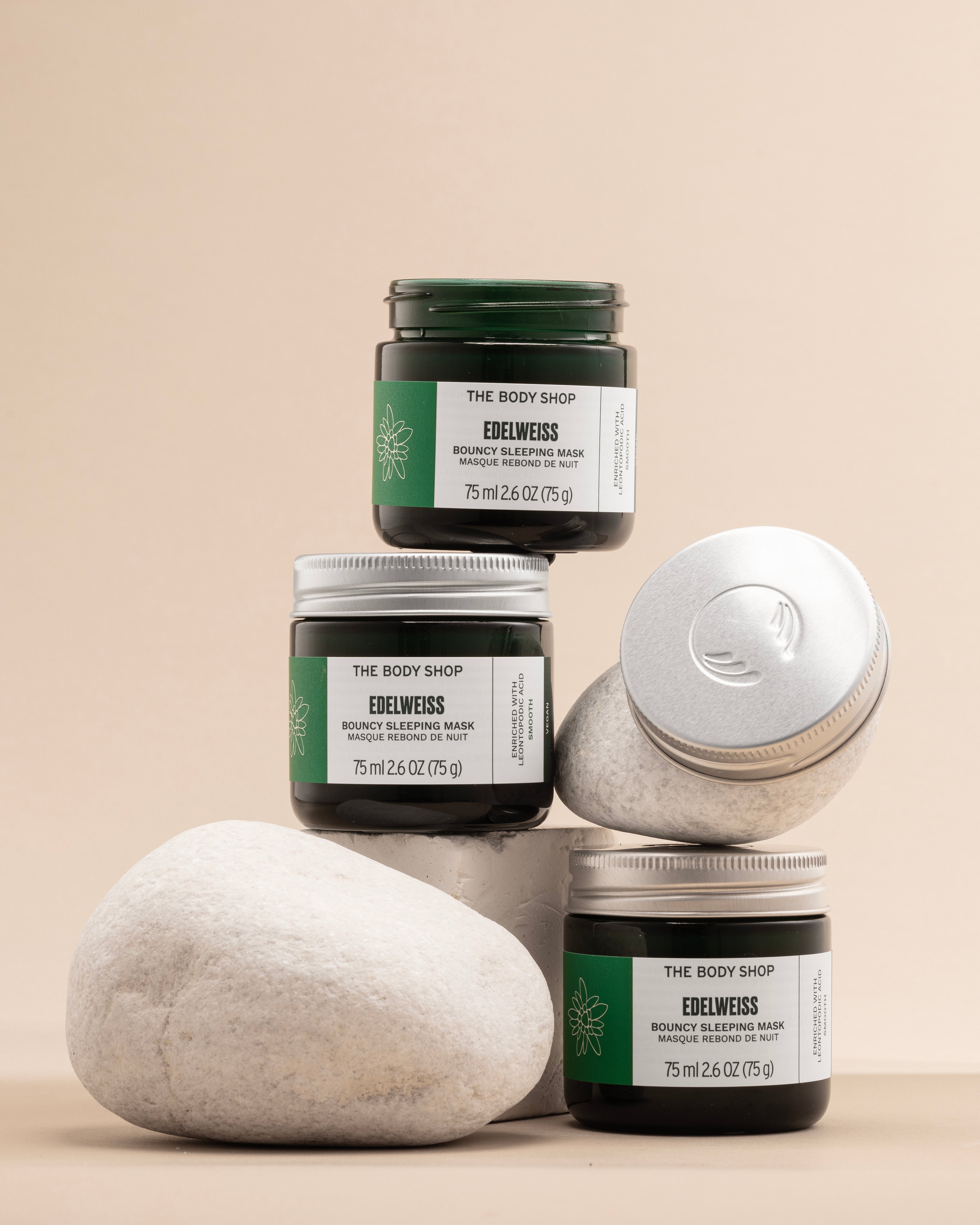 The Body Shop Edelweiss Bouncy Sleeping Mask 75ml displayed in an artistic arrangement of jars on neutral stones.