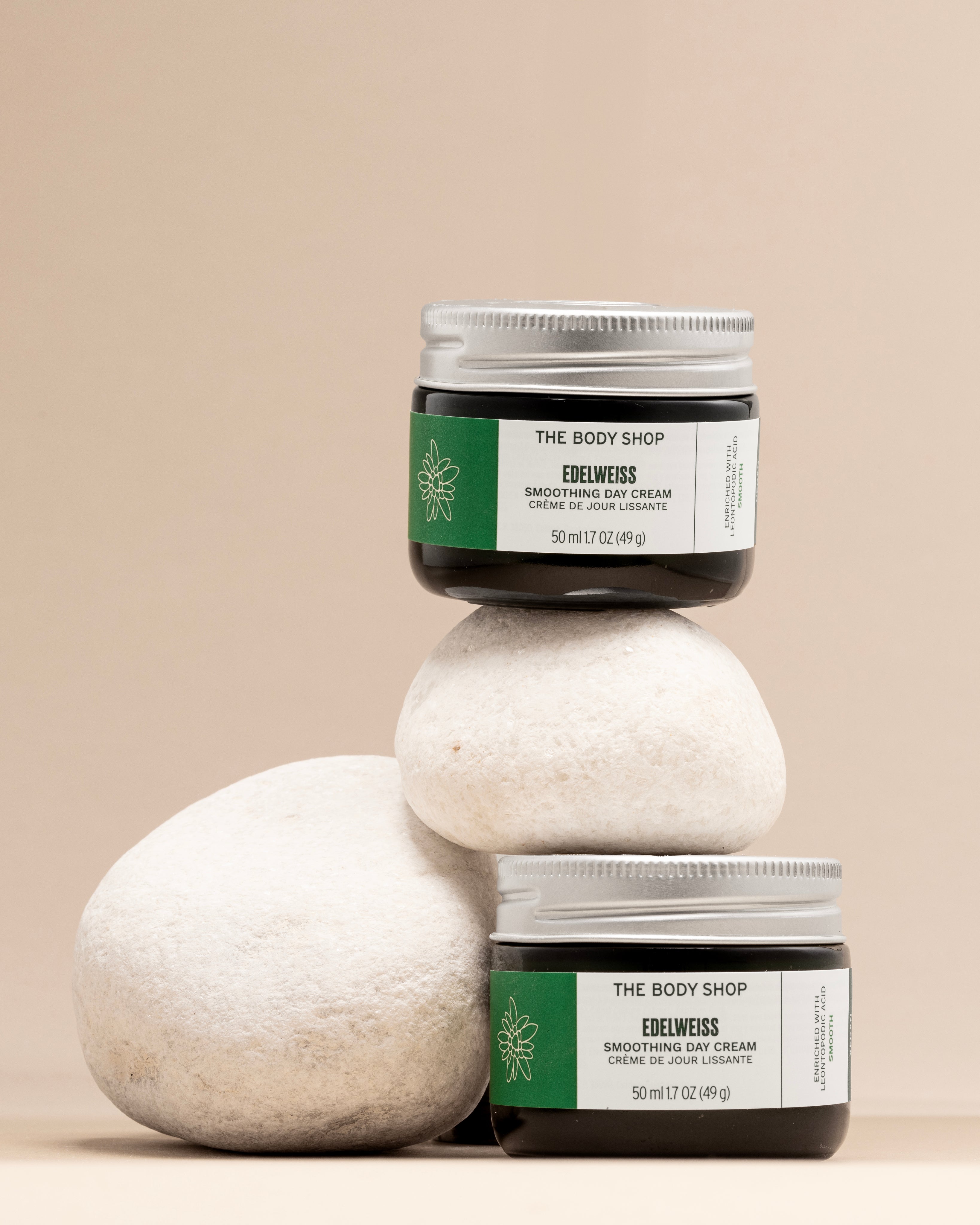 Stylish arrangement of The Body Shop Edelweiss Smoothing Day Cream 50 ML on smooth stones against soft beige backdrop