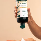 Hand pouring The Body Shop Ginger Scalp Care Conditioner 440 ML into palm against a neutral background.