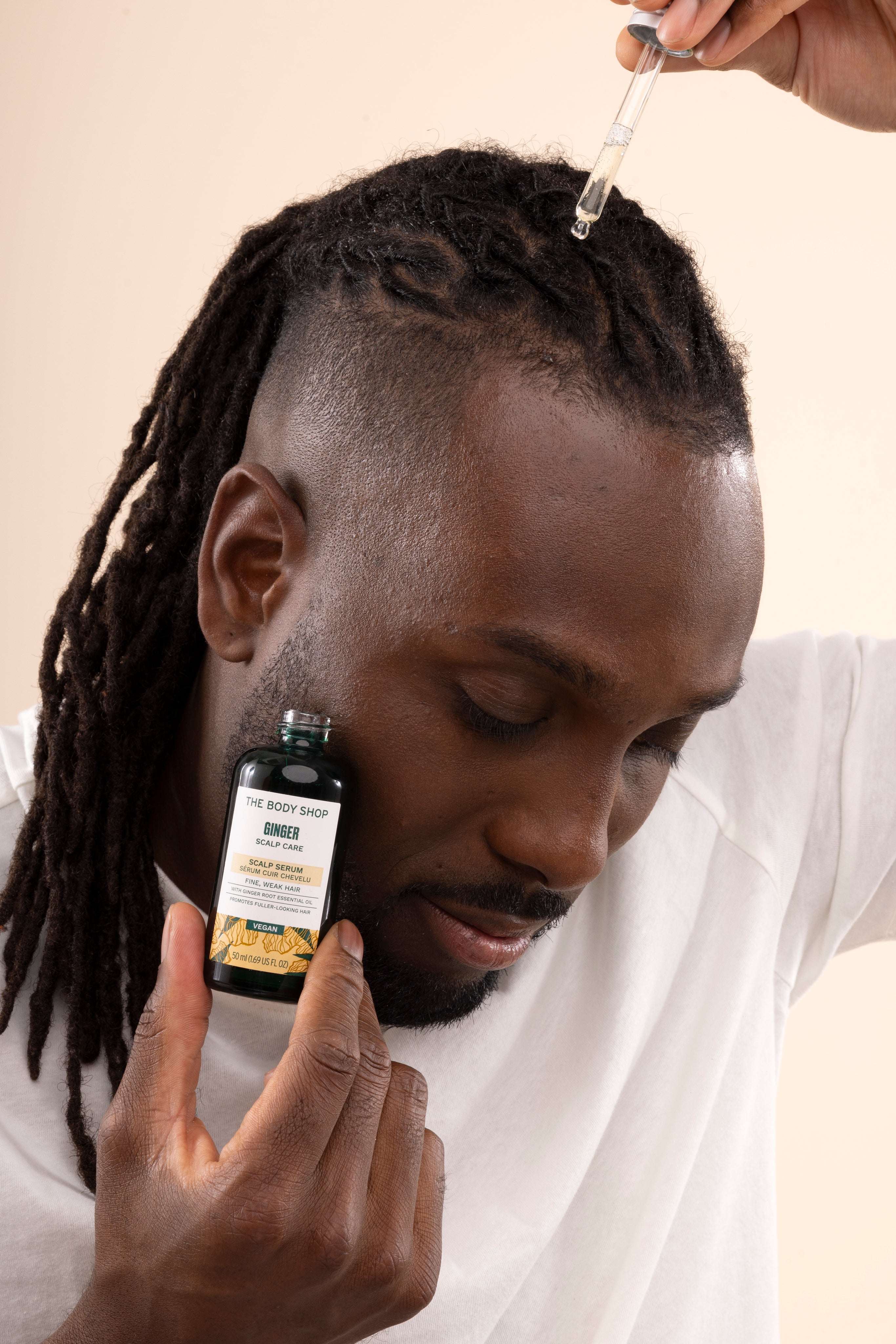 Man applying The Body Shop Ginger Scalp Serum 50 ML in studio setup with backdrop