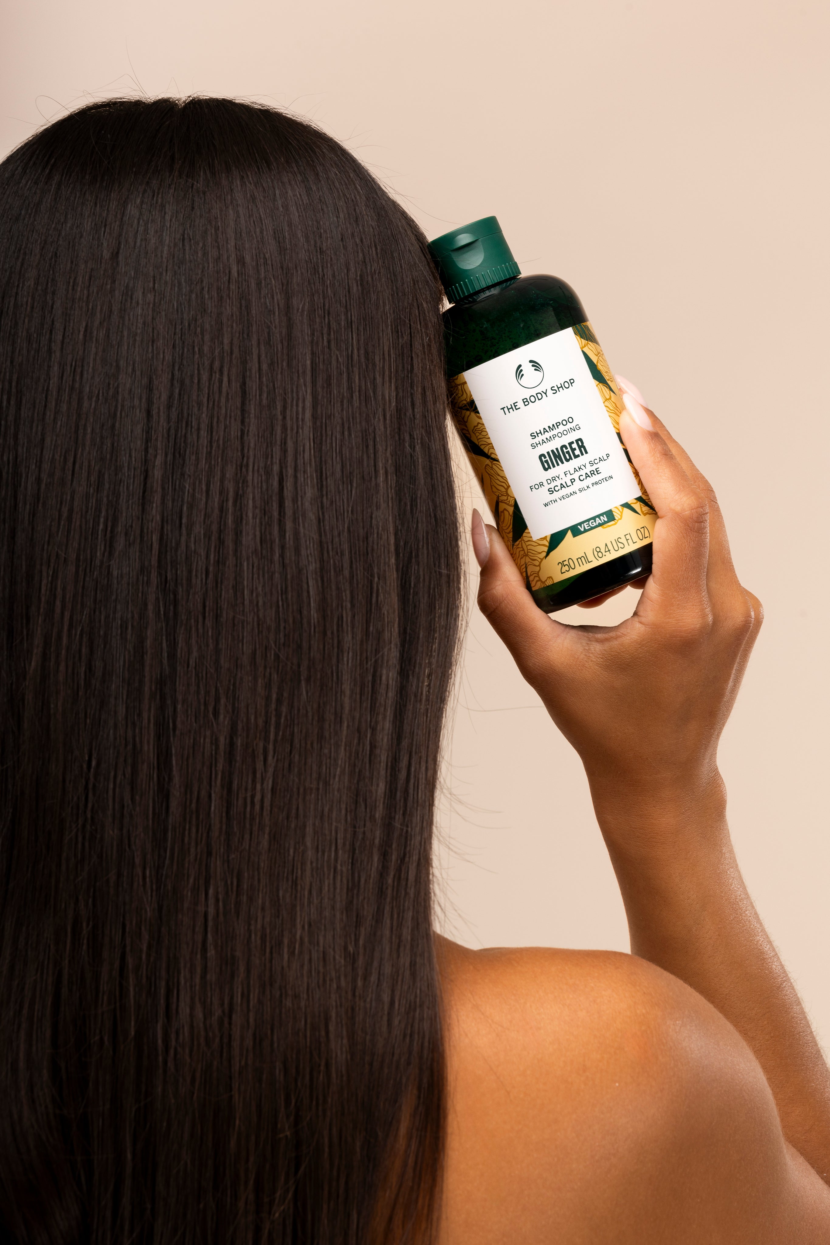 Woman holding The Body Shop Ginger Shampoo 250 ML against soft neutral background