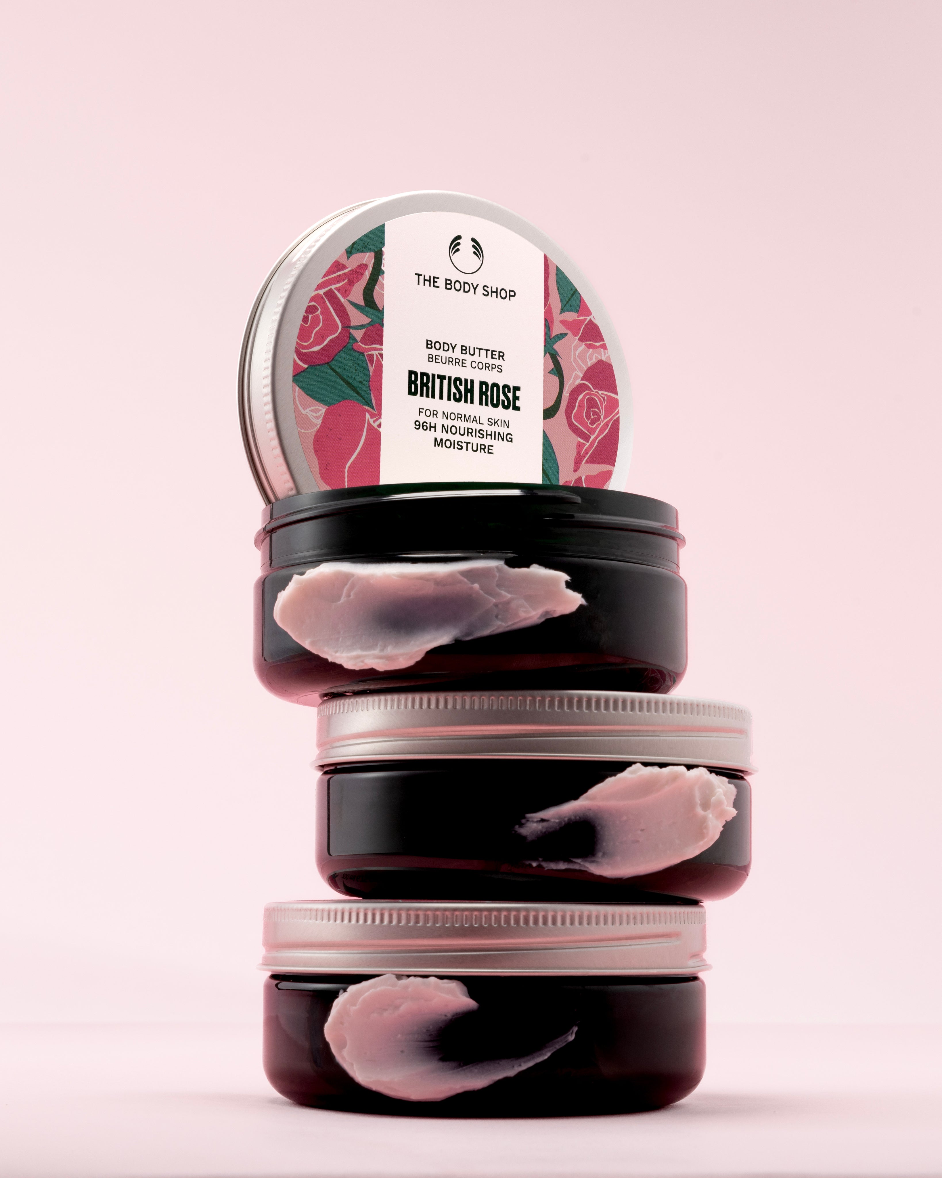 A stack of The Body Shop British Rose Body Butter 200ml against a soft pink backdrop.