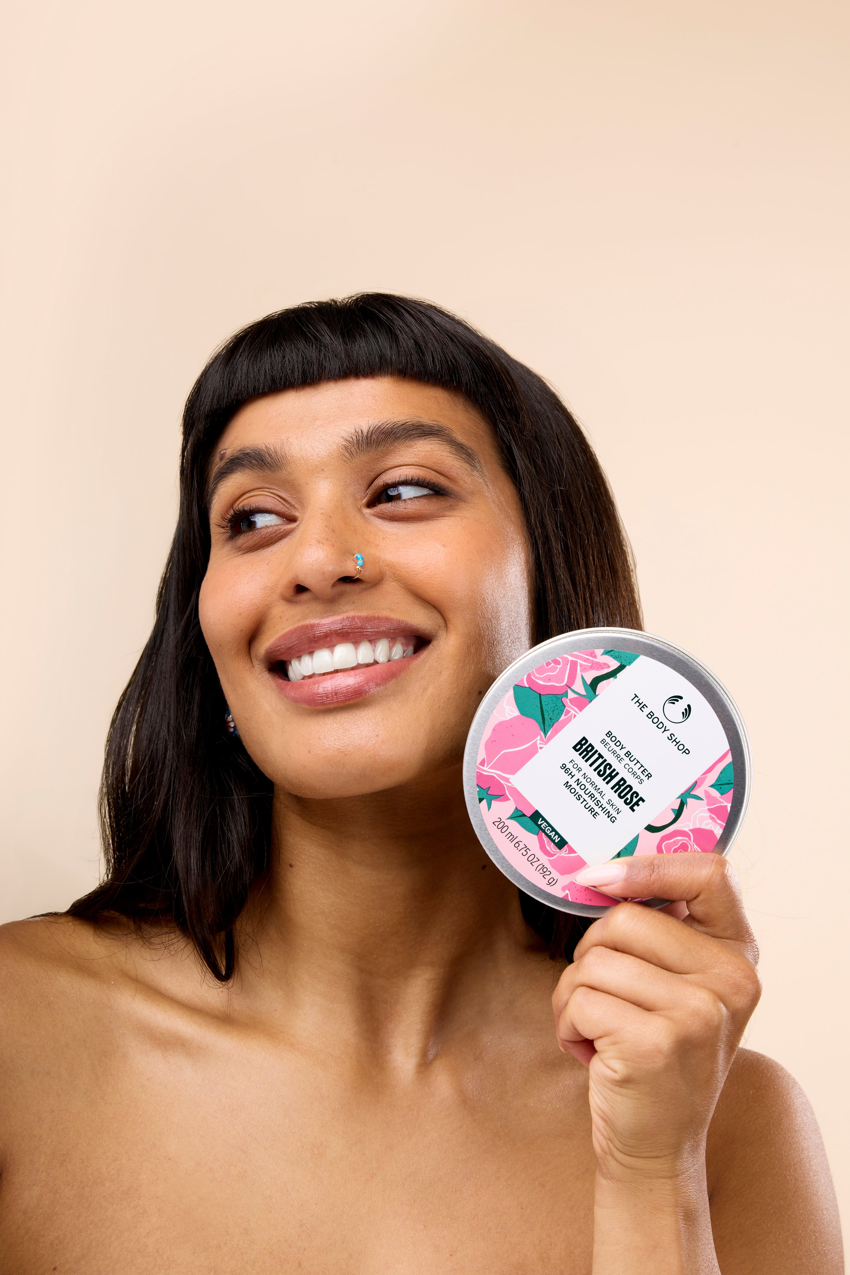 Woman smiling while holding The Body Shop British Rose Body Butter 200 ML against a soft, neutral background.