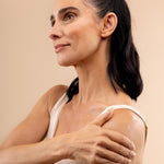 Woman applying Almond Milk Body Butter 200 ML against a soft, neutral backdrop, showcasing its moisturizing texture.