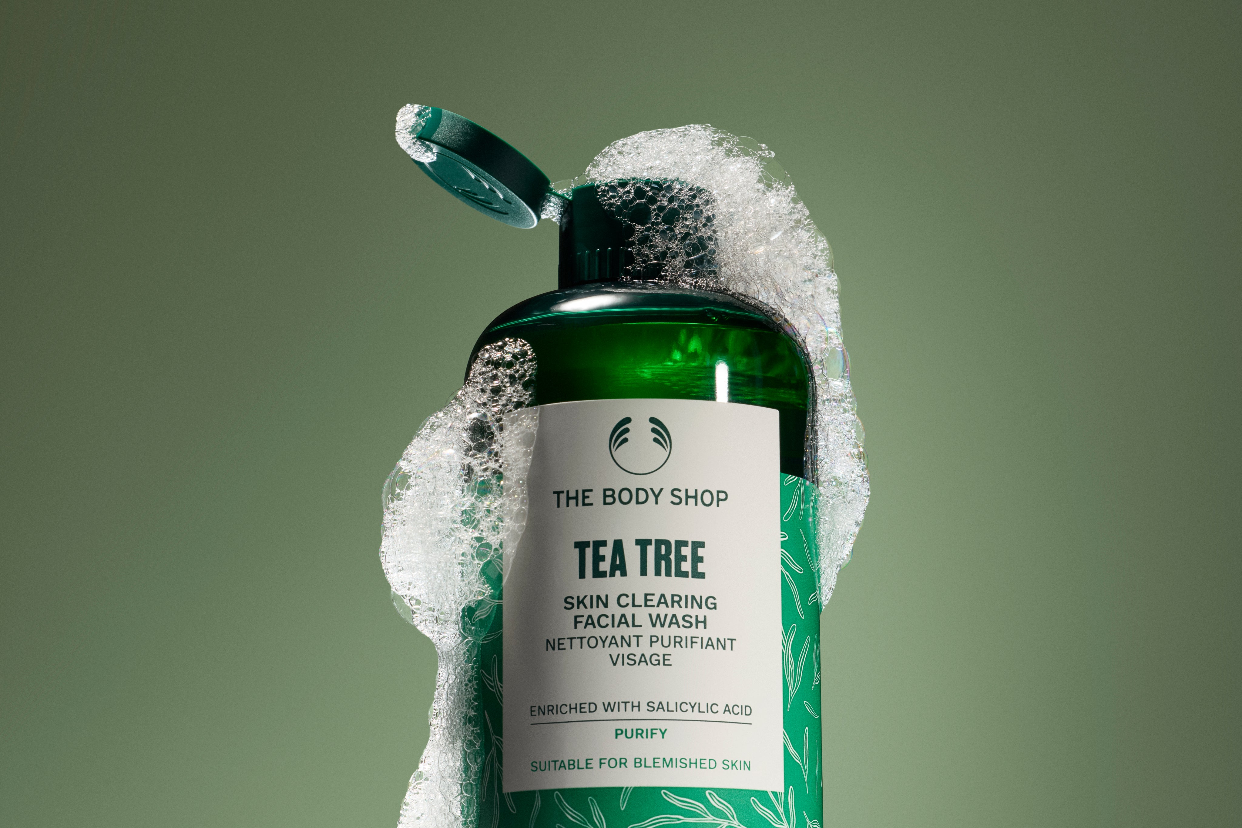 Green bottle of The Body Shop Tea Tree facial wash with a green background