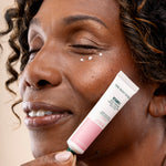Woman applying The Body Shop Vitamin E Crème Crème des Yeux 15 ML to her face, showcasing product texture on skin.