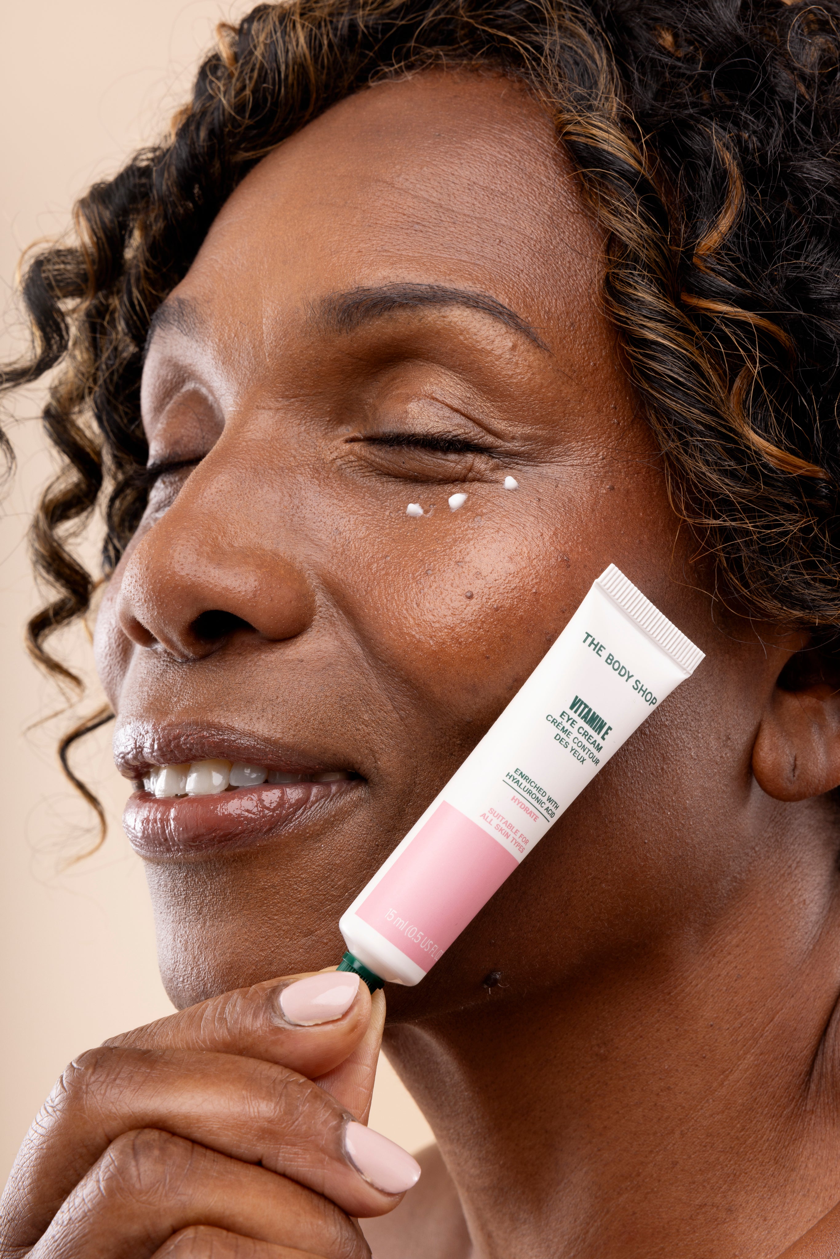 Woman applying The Body Shop Vitamin E Crème Crème des Yeux 15 ML to her face, showcasing product texture on skin.