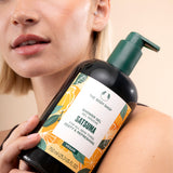 Young woman holding The Body Shop Satsuma Shower Gel 750 ML showcasing the product against her arm in a natural setting.