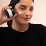Woman applying The Body Shop Aloe Soothing Night Cream 50ml in a studio setting with a soft backdrop.