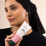 Woman holding The Body Shop Vitamin E Gentle Facial Wash 125ml against soft pastel background highlighting hydration.