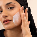 Woman applying Vitamin E Gentle Face Wash 125 ML on her cheek with creamy texture visible on skin against studio backdrop.