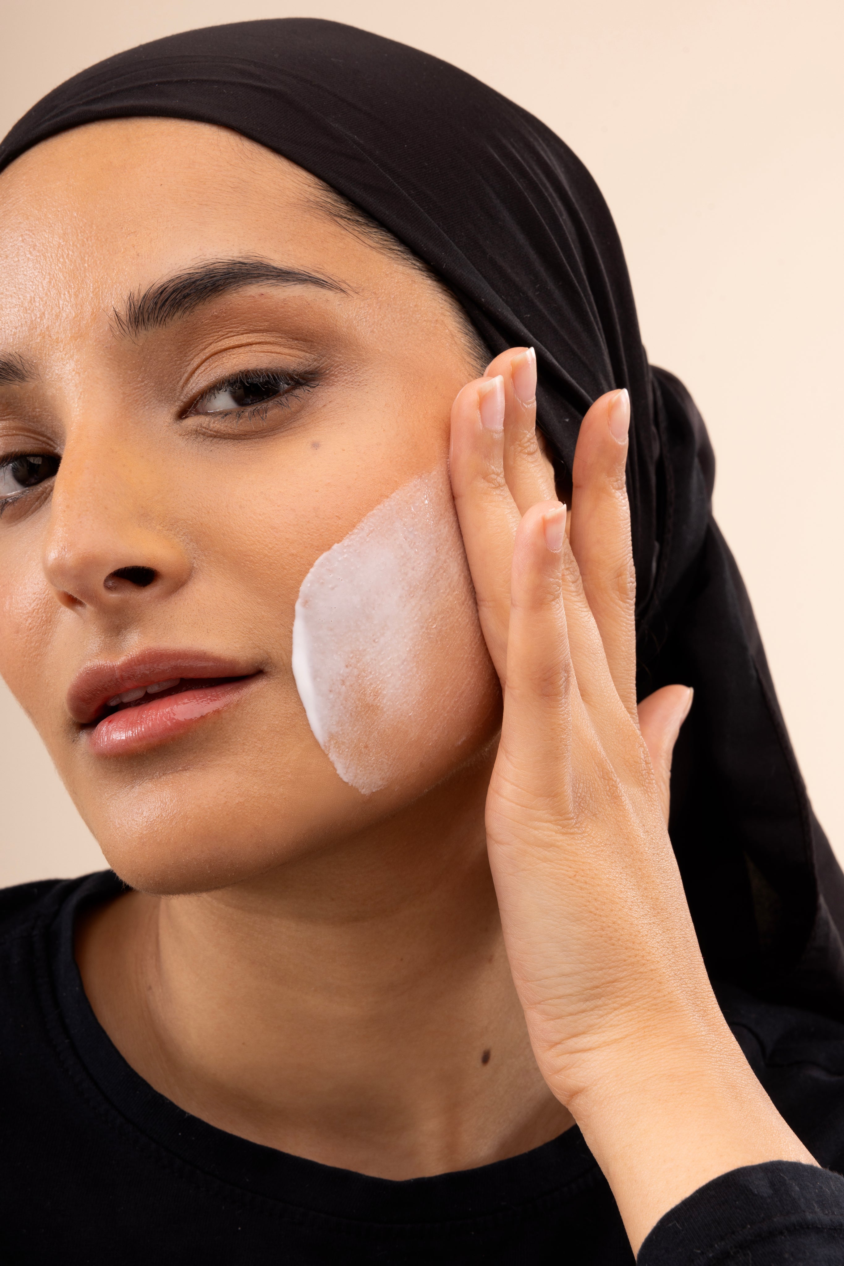 Woman applying Vitamin E Gentle Face Wash 125 ML on her cheek with creamy texture visible on skin against studio backdrop.