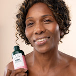 Woman smiling while holding The Body Shop Vitamin E Cream Cleanser 250 ML against soft, neutral background
