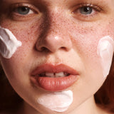 Close-up of a person's face with The Body Shop Vitamin E Day Cream on their cheeks and chin.