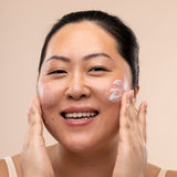 Woman applying The Body Shop Vitamin E Day Cream to her face against a beige background