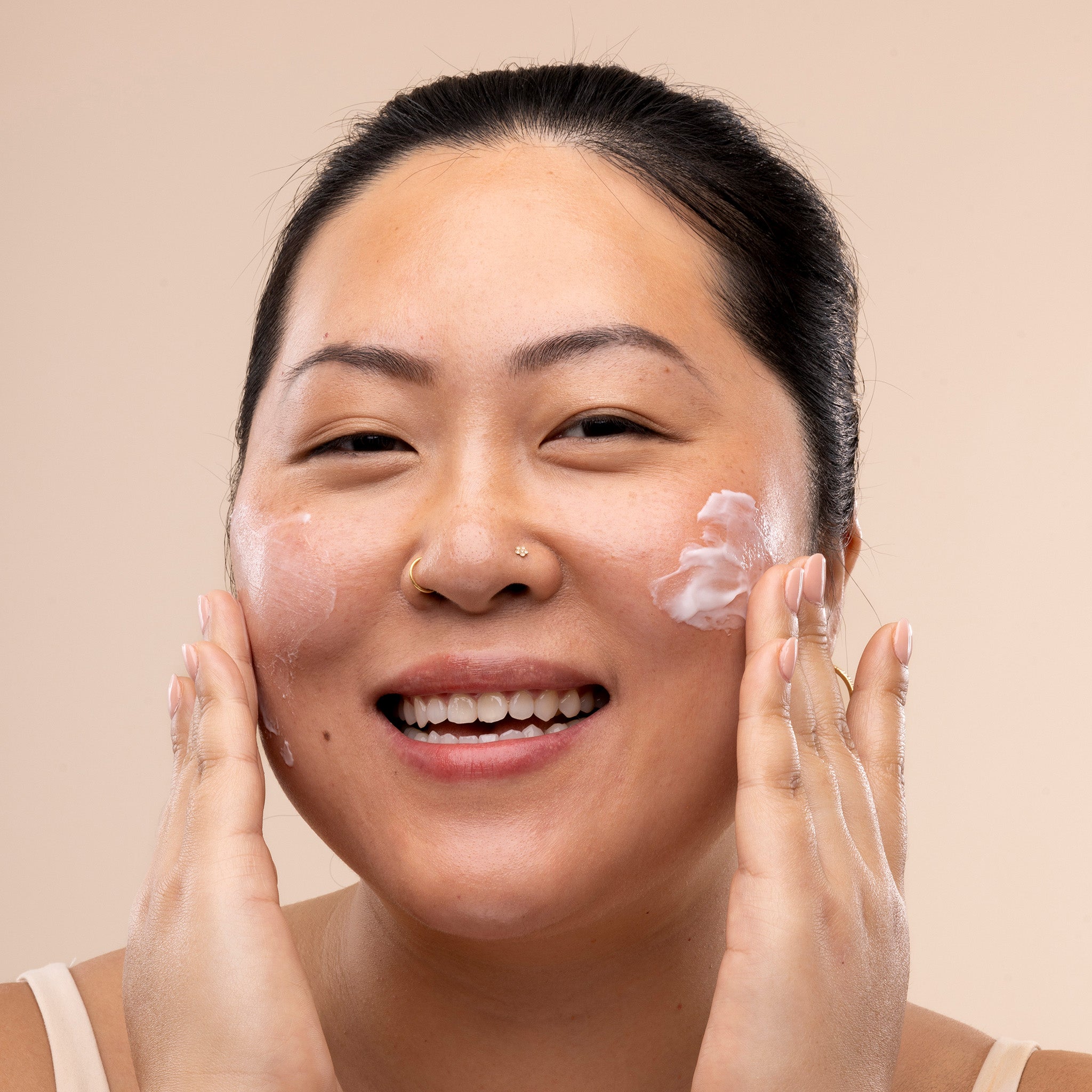 Woman applying The Body Shop Vitamin E Day Cream to her face against a beige background
