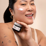Woman applying The Body Shop Vitamin E Moisture Cream in a well-lit setting with a soft background