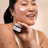 Woman applying The Body Shop Vitamin E Moisture Cream in a well-lit setting with a soft background