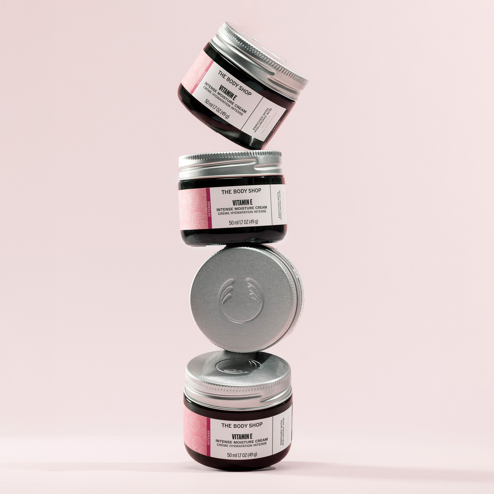 Stack of four jars of The Body Shop Vitamin E Intense Moisture Cream with a pink background