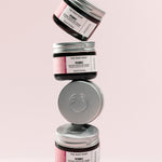 Stack of The Body Shop Vitamin E Intense Moisture Cream 50 ML jars against a soft pink background
