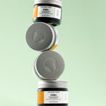 Three jars of The Body Shop Vitamin C Glow Boosting Moisturiser 50 ML stacked on a textured surface against a soft green back